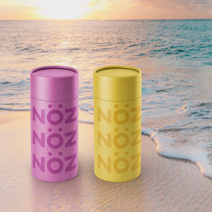 Bottles from Noz sunscreen in yellow and purple colors on the beach